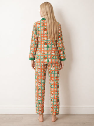 A teenage girl stands with her back to the camera wearing a two-piece pyjama set with a colourful geometric pattern of orange, green, and beige squares, featuring a green collar and cuffs.