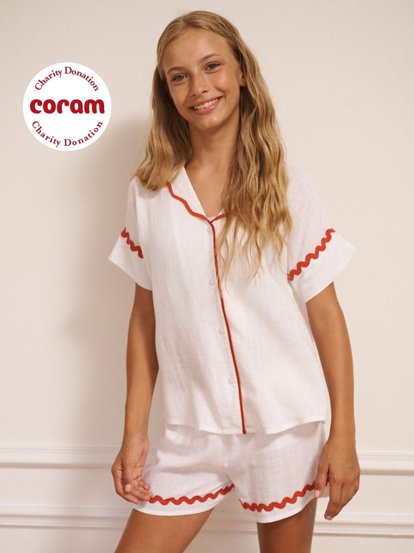 Tween wearing a white pyjama set with red trim against a plain background.