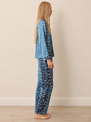 A teenager stands in profile wearing a matching two-piece pyjama set with a blue base and white abstract speckled pattern, photographed against a plain beige wall and light wood floor.
