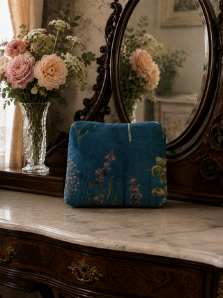 Blue printed velvet cosmetic bag on a marble surface with a decorative mirror and flowers in the background