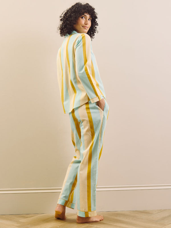 Woman wearing a striped pajama set against a beige wall. Back Detail. 