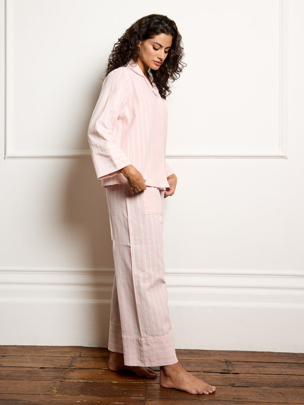 Woman wearing a light pink pajama set standing against a white wall.