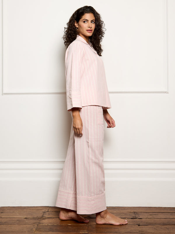 Woman wearing a light pink outfit standing against a white wall.