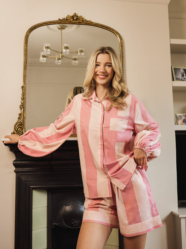 Woman wearing a pink and white striped pyjama set standing in front of a mirror.