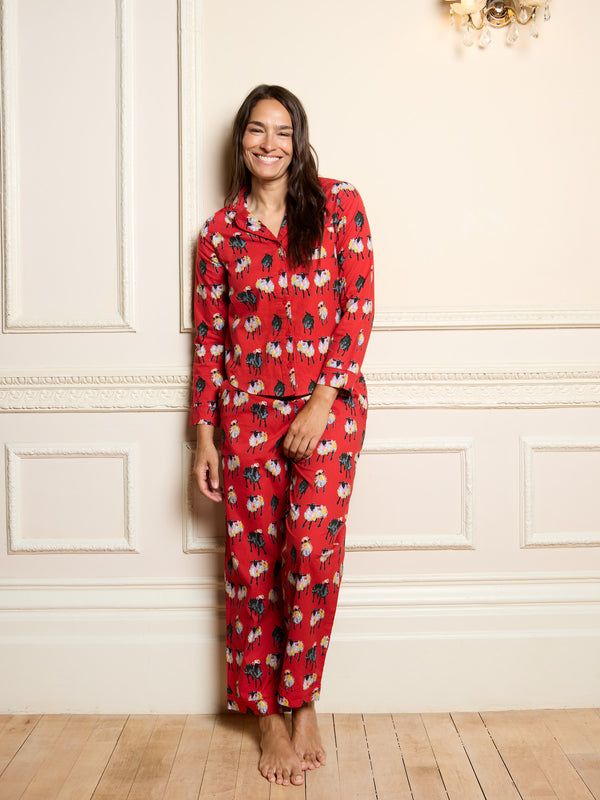 Woman wearing a red pyjama set with a sheep pattern in a room with white walls and wooden flooring.