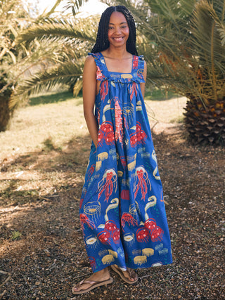A woman standing outdoors in a navy nightdress with a square neck and long frill, featuring a red and blue ocean and coral print.