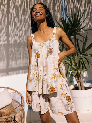 A woman standing in an outdoor setting wearing a cream-coloured linen mix ruched cami top with a celestial print, paired with matching shorts.