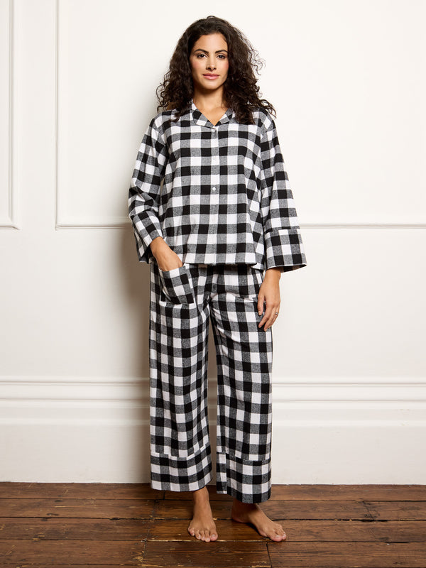 Woman wearing a black and white checkered pajama set against a white wall.