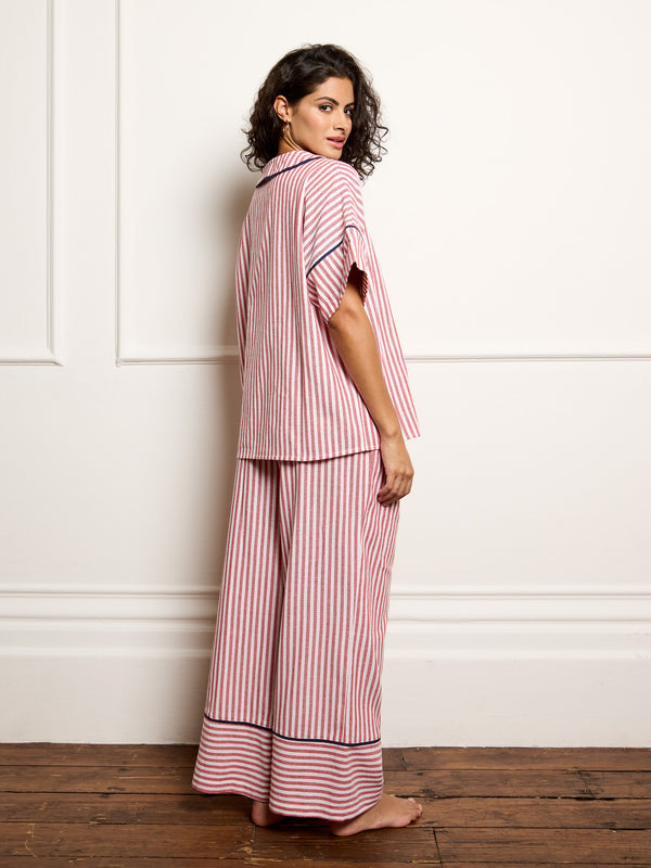 Woman wearing a pink and white striped pajama set against a white wall.