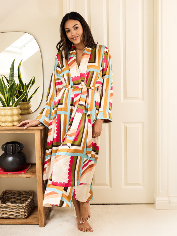 Woman wearing a colourful patterned dressing gown robe standing in a room with a mirror and plants.
