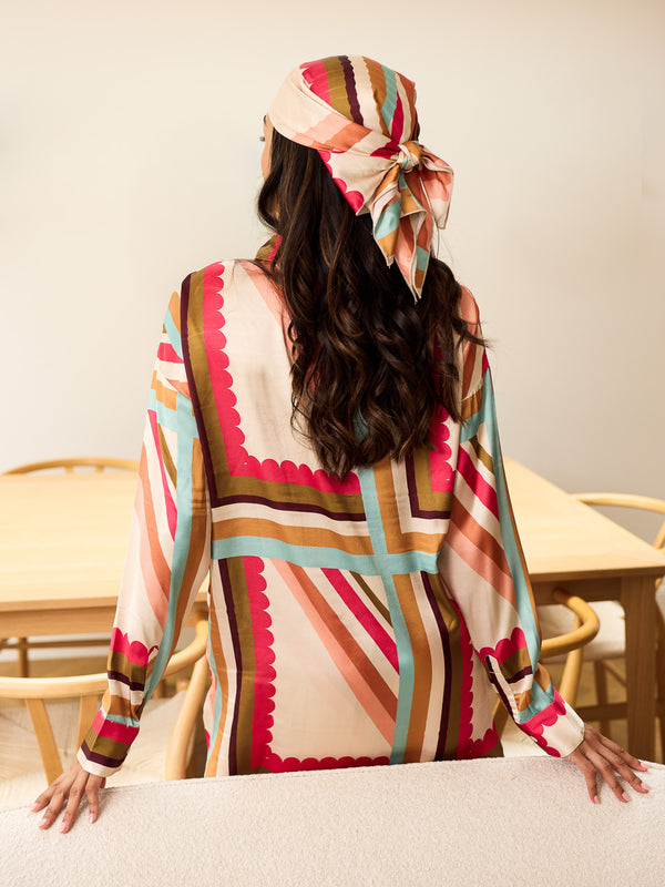Woman wearing a colorful patterned outfit with a headscarf in a room with chairs and a table.
