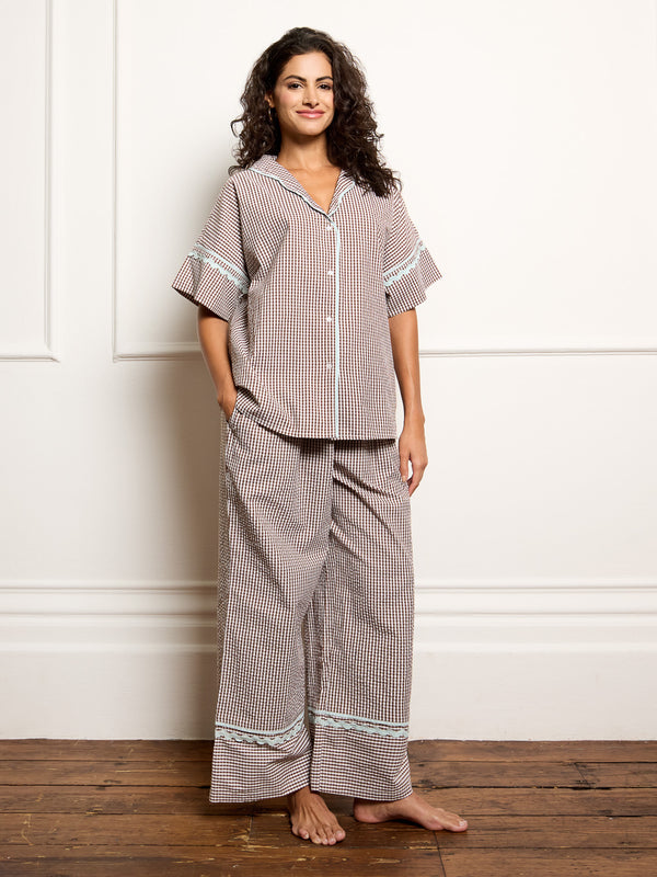 Woman wearing a gingham pyjama set against a white wall.