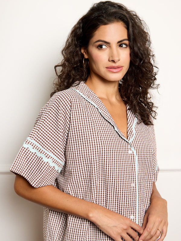 Woman wearing a gingham pyjama set against a white wall.