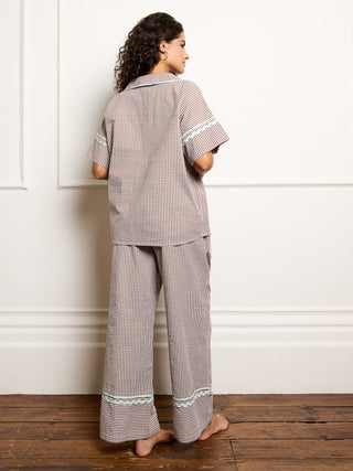 Woman wearing a gingham pyjama set against a white wall.