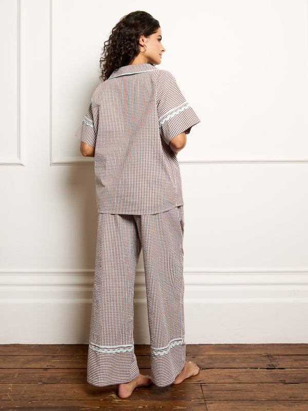 Woman wearing a gingham pyjama set against a white wall.