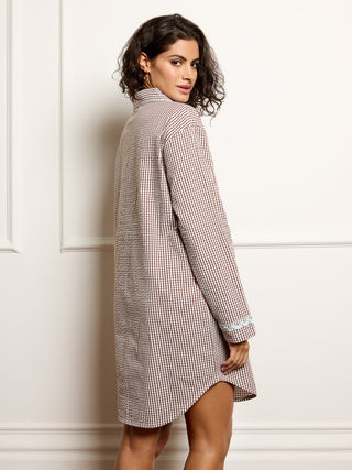 Woman wearing a gingham nightie against a white wall