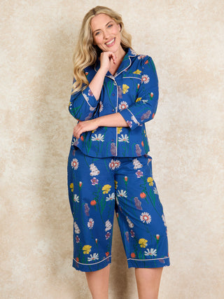 A woman standing and posing in long sleeve capri pyjamas with a field flower print on a navy base.