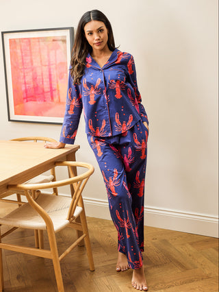 Woman in a blue and red pajama set standing in a room with wooden furniture and a painting on the wall.