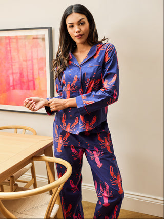 Woman wearing a blue pajama set with red lobster pattern in a room with a table and wall art.