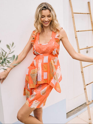 A woman wearing terracotta-colored cotton voile shorts with a Moroccan fruits print, paired with a matching button-down shirt.