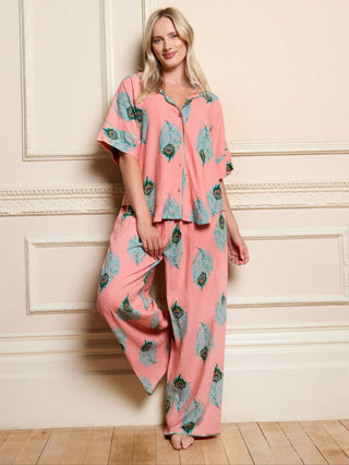 Woman wearing a pink peacock pyjama set in a room with white walls and wooden flooring.