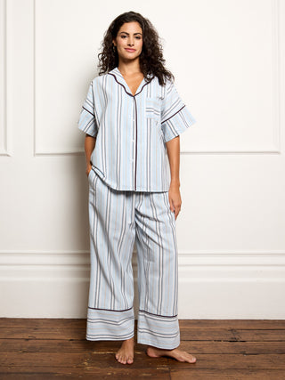Woman wearing a light blue pyjama set with stripes against a white wall.