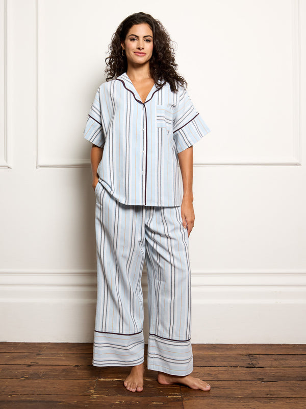 Woman wearing a light blue pyjama set with stripes against a white wall.