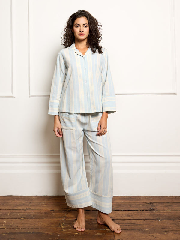 Woman wearing a light blue striped pyjama set against a white wall.