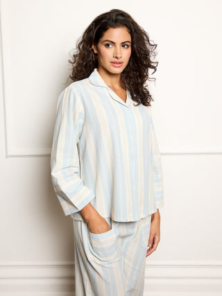 Woman wearing a light blue and white striped pyjama set against a white background