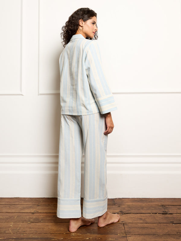 Woman wearing a light blue and white striped pyjama set against a white wall.