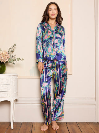 Woman wearing a colourful floral pyjama set in a room with a white dresser and flowers.