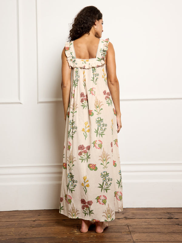 Woman wearing a floral night dress standing against a white wall. Back Detail