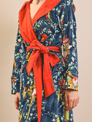 A close-up of a person wearing a long-sleeve floral dressing gown robe with a bold red-orange solid inner collar, waist tie, and matching tie, over a navy blue floral base fabric.