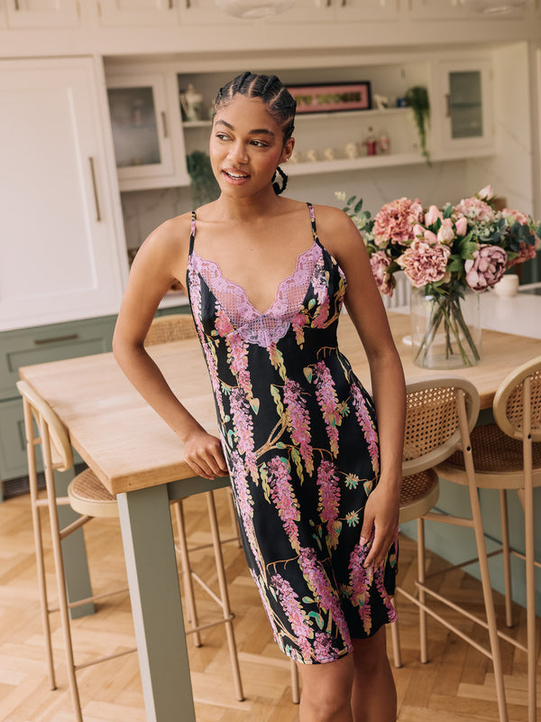woman wearing black satin mini night dress with wisteria pattern and purple lace standing in a kitchen