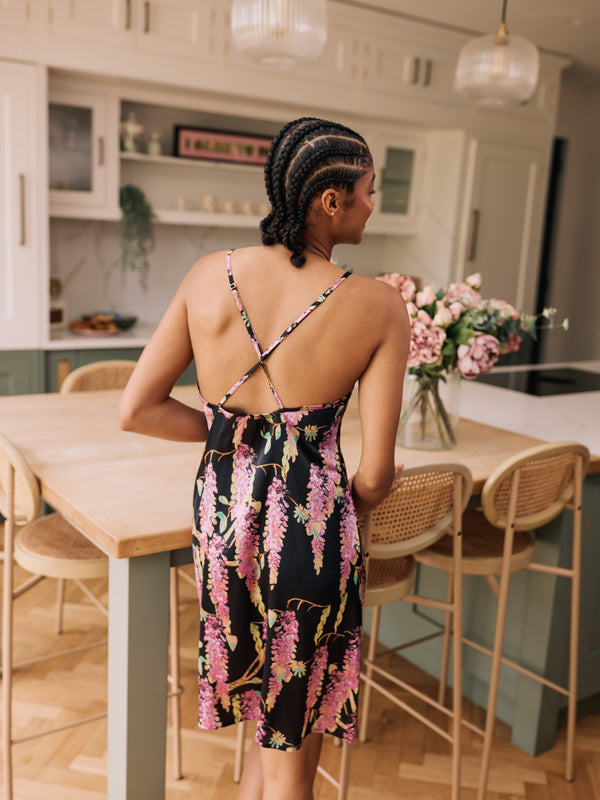 woman wearing black satin mini night dress with wisteria pattern and crossed straps at the back