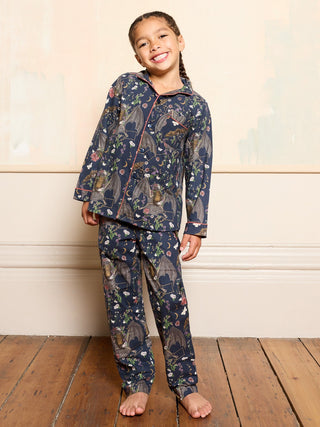 Young girl wearing a bat halloween patterned pyjama set on a wooden floor with a neutral wall background