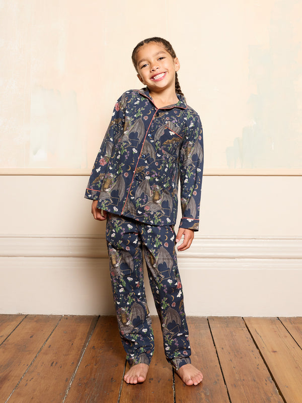 Young girl wearing a bat halloween patterned pyjama set on a wooden floor with a neutral wall background