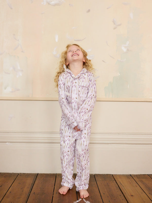 Child wearing a floral lilac pyjama set standing against a light-coulored wall with feather decorations.