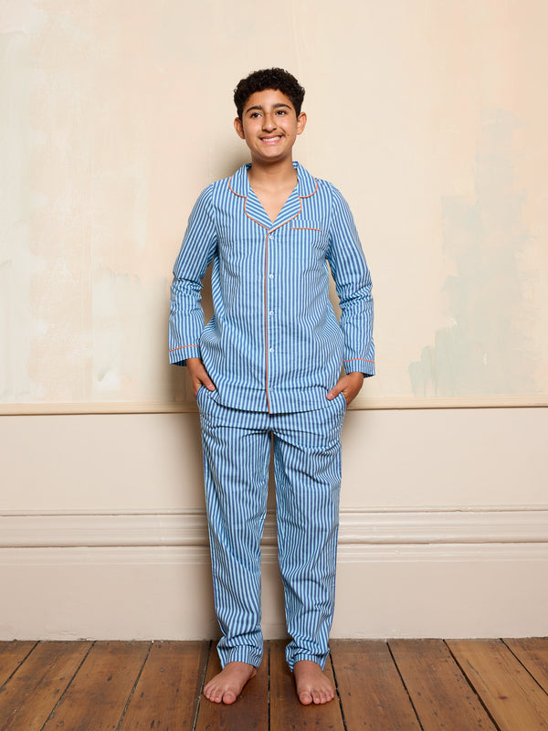 Boy wearing blue striped pyjamas standing against a beige wall.