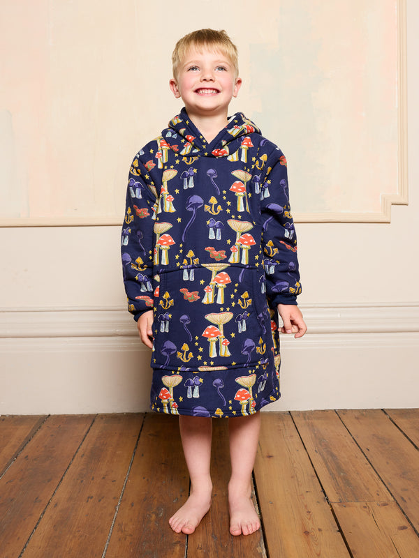 Child wearing a navy blue hooded robe with colourful mushroom patterns on a wooden floor.