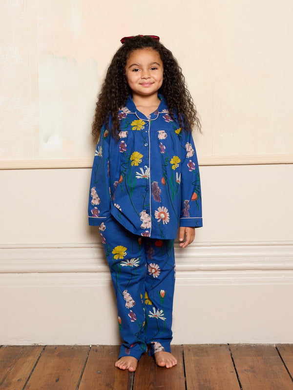 Child wearing a blue floral pyjama set standing against a white wall.