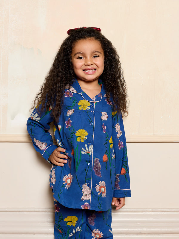 Young girl wearing a blue floral pyjama set against a beige wall.