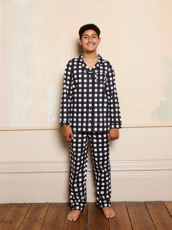 Older child wearing black gingham pyjama set smiling against a neutral background