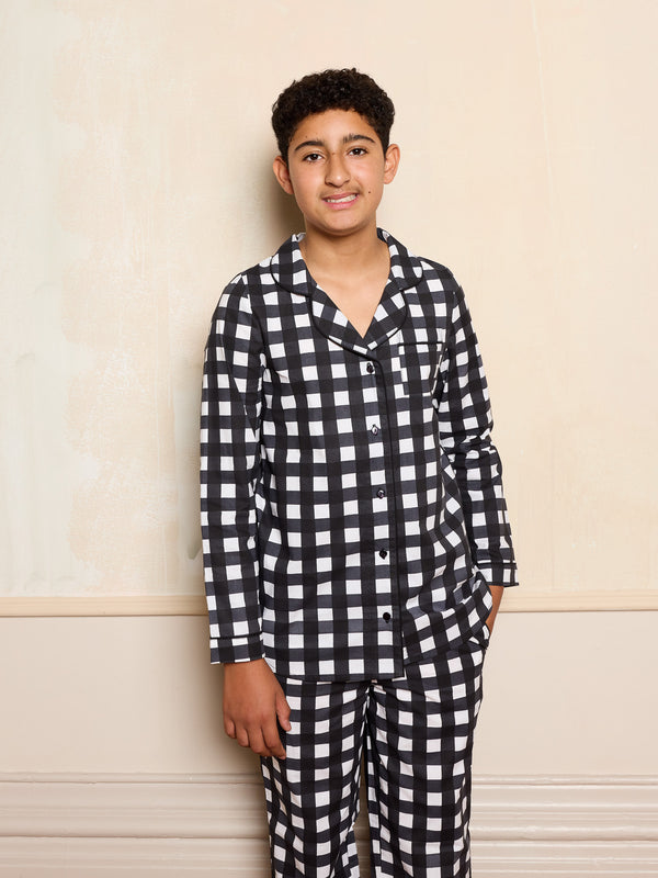 Older child wearing black gingham pyjama set smiling against a neutral background