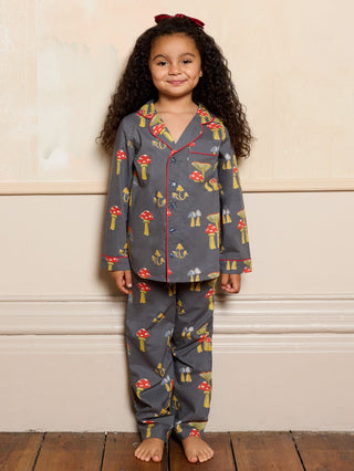 Child wearing a grey mushroom patterned pyjama set standing against a beige wall.