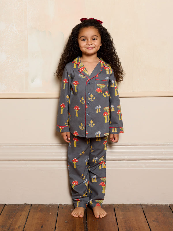 Child wearing a grey mushroom patterned pyjama set standing against a beige wall.