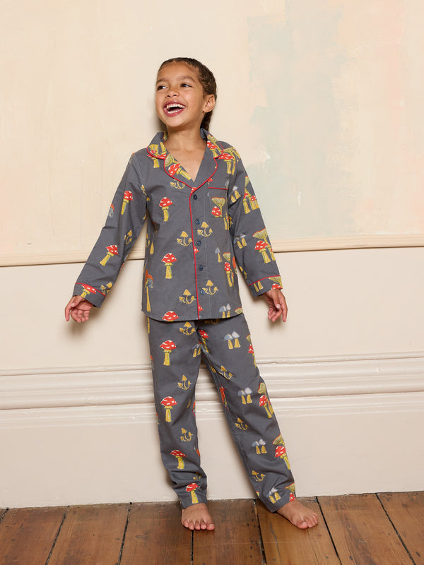 Child wearing a grey mushroom patterned pyjama set standing against a beige wall.