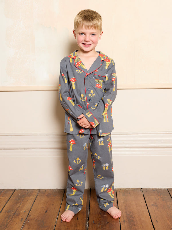 Child wearing a grey mushroom patterned pyjama set standing against a beige wall.