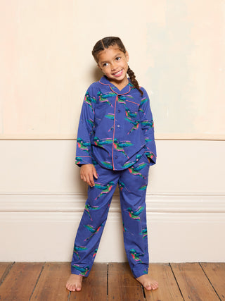 Young girl wearing blue pyjamas with colourful hummingbird pattern standing on a wooden floor.