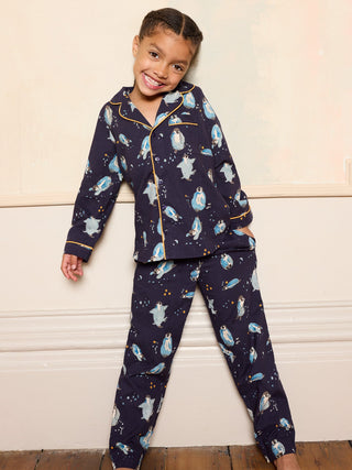 Child wearing a navy blue pyjama set with penguin print smiling against a neutral wall.